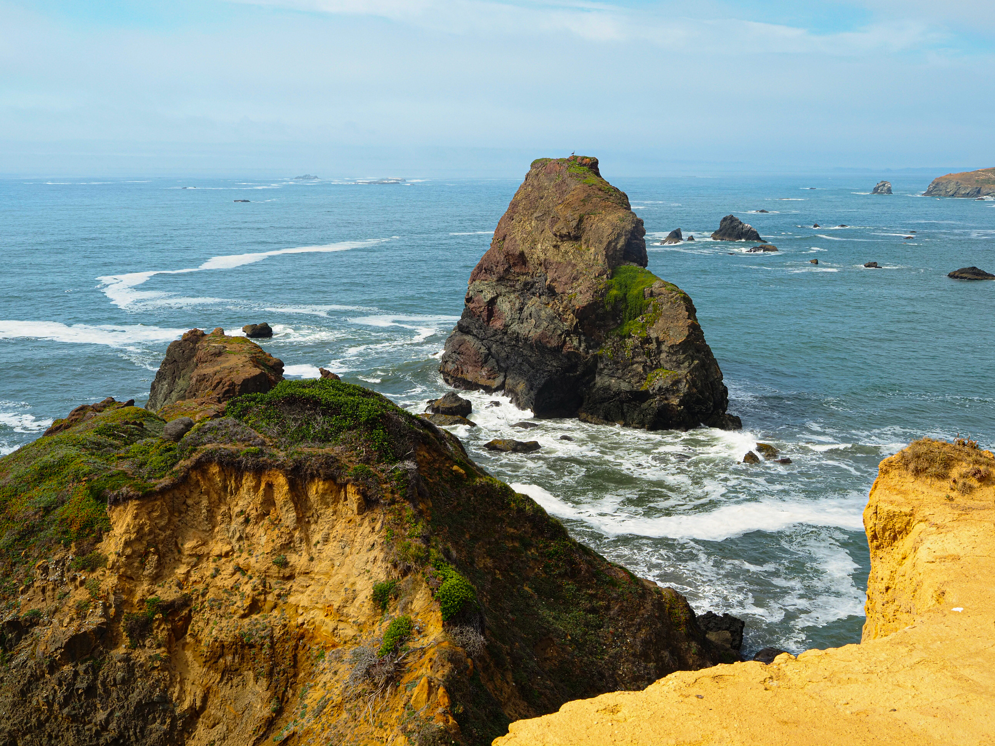 A triangular rock juts out of the blue Pacific ocean 