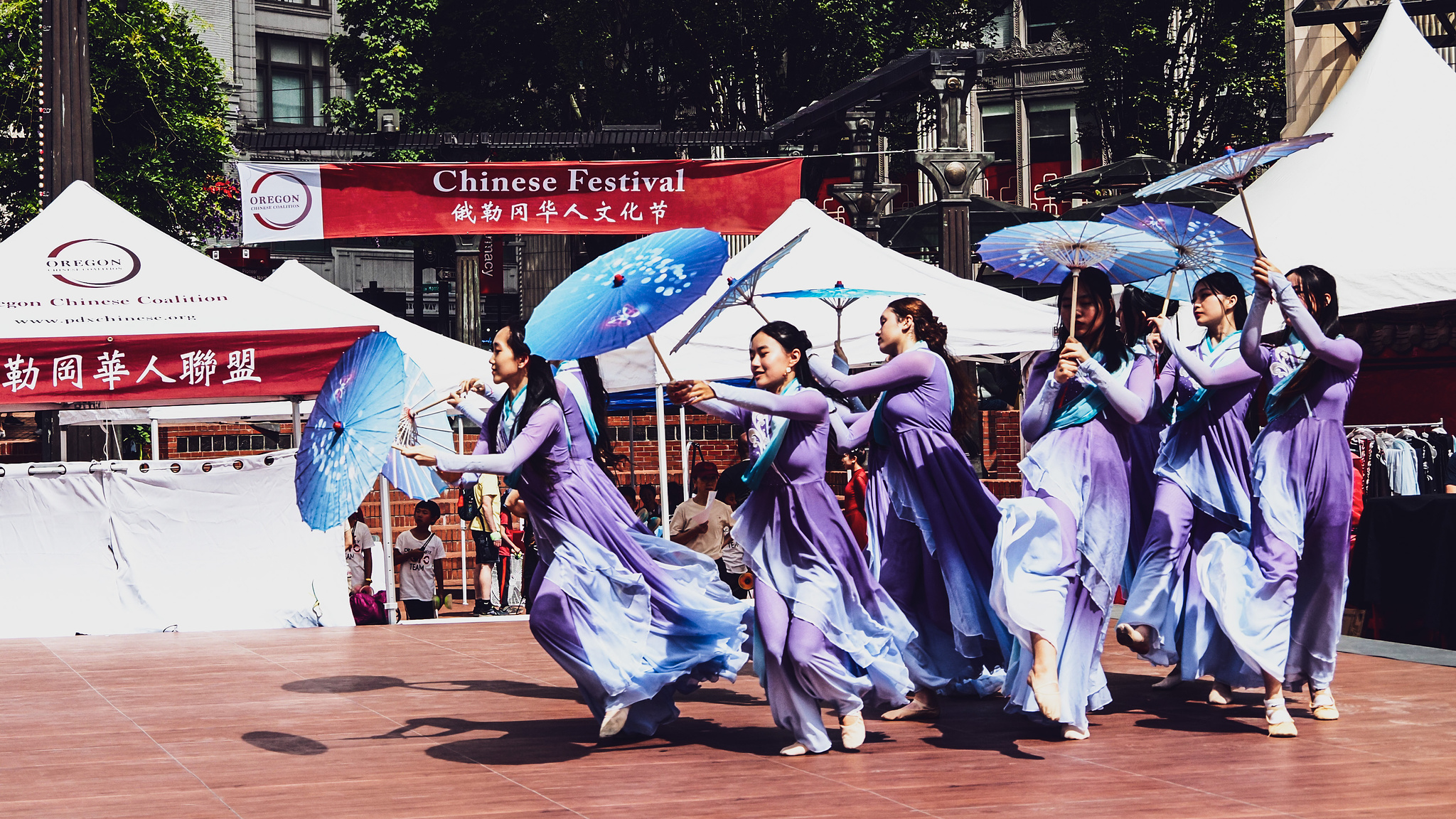 Chinese dancers in purple robes run onto the square holding blue parasols