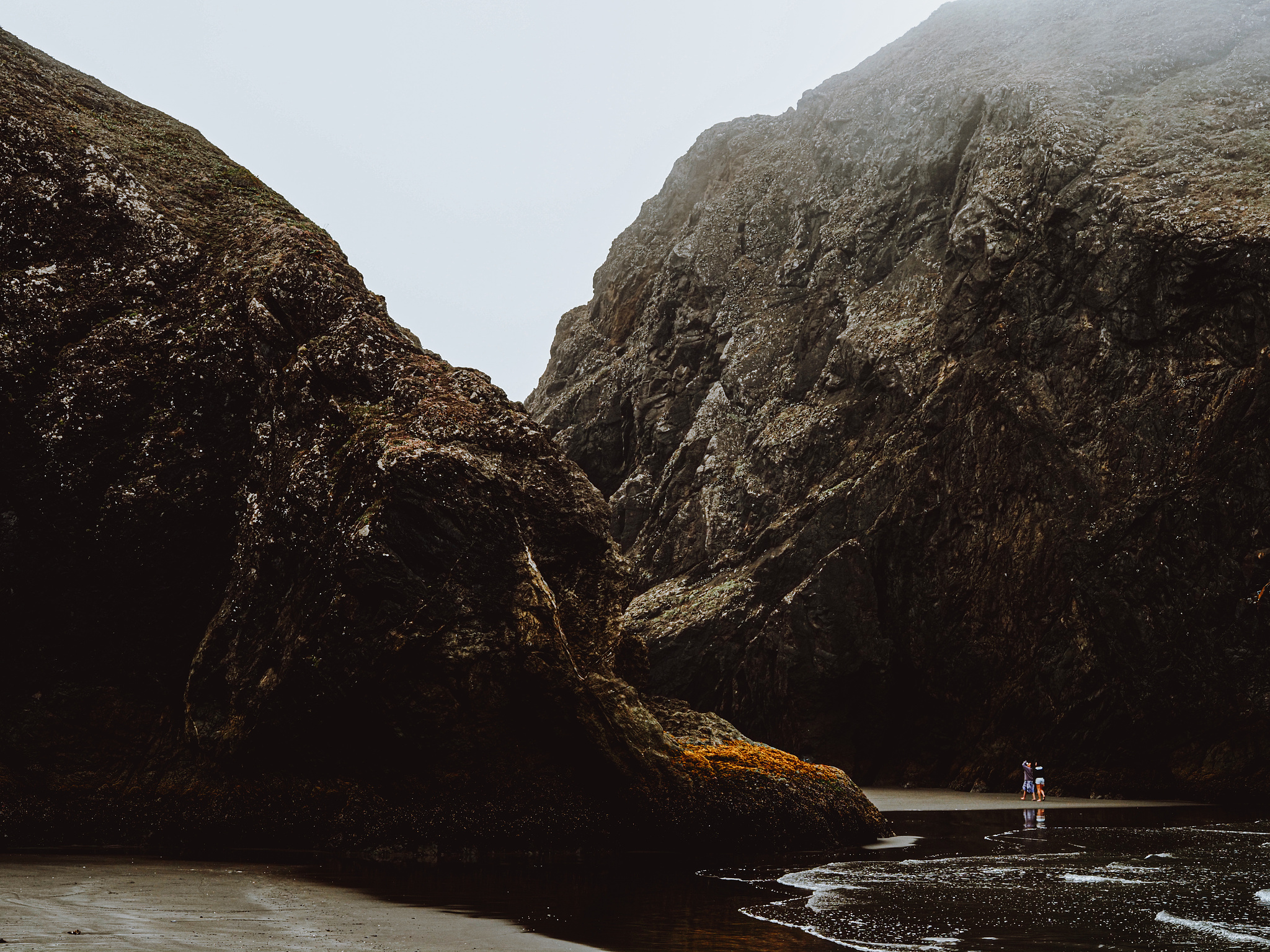 Two women dwarfed by giant rocks in the ocean