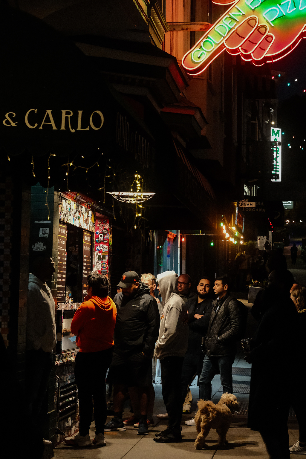 People standing under a neon sign for Golden Boy pizza