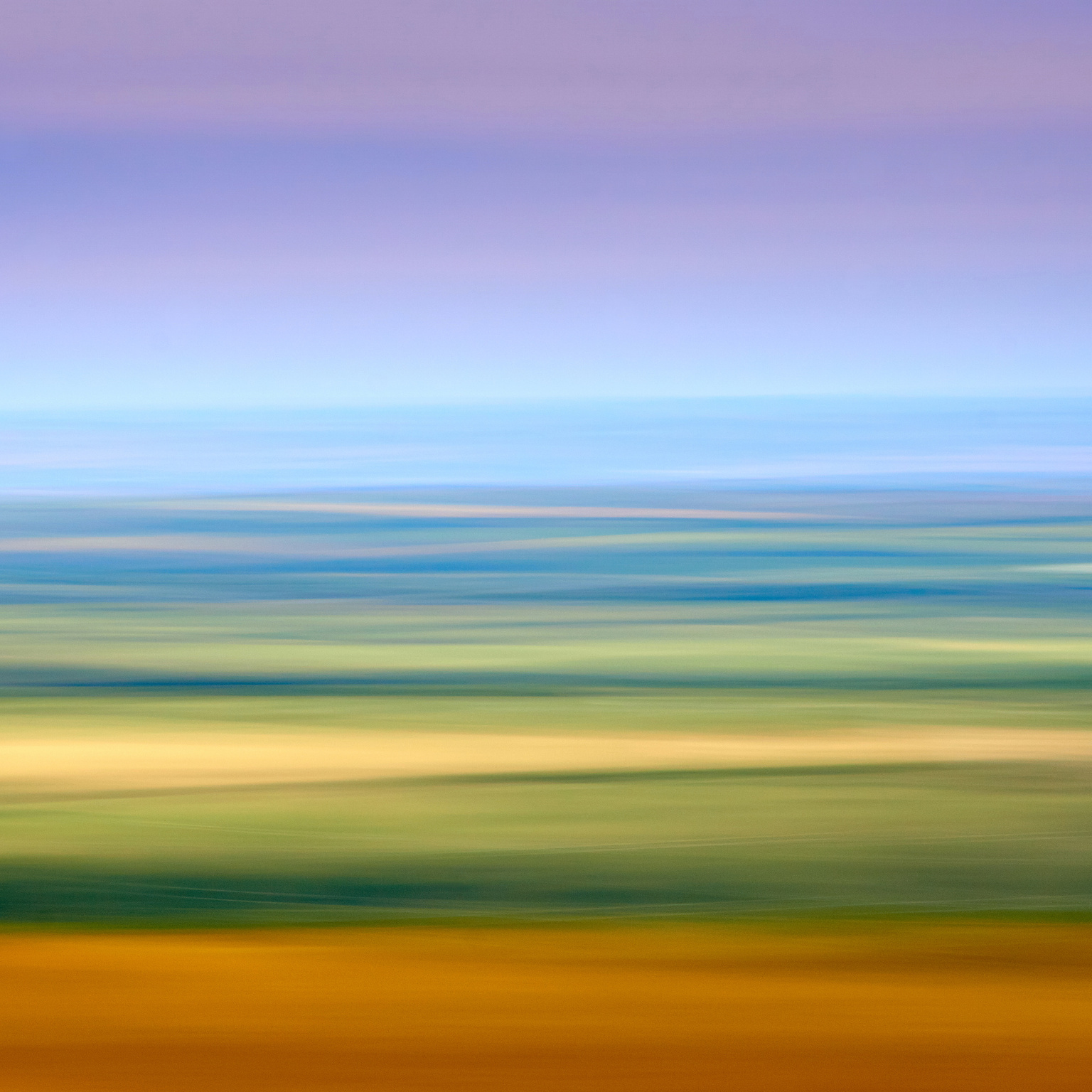 Square abstract image consisting of horizontal waves of colour, ranging from the bottom of the frame oranges, through yellows, greens and finally pinky blues at the top. It is a landscape view over fields of different crops but smeared detail using a camera movement technique.