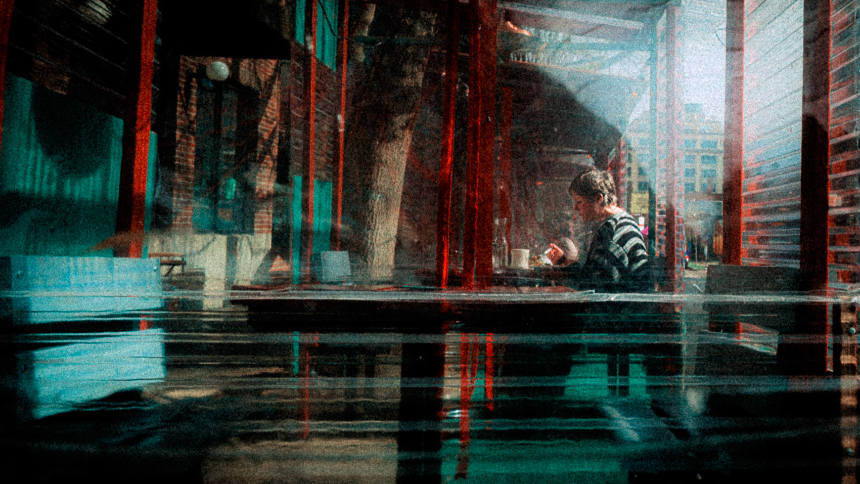 A woman eats alone under a sidewalk shelter, the view is blurred by layers of protective plastic. 