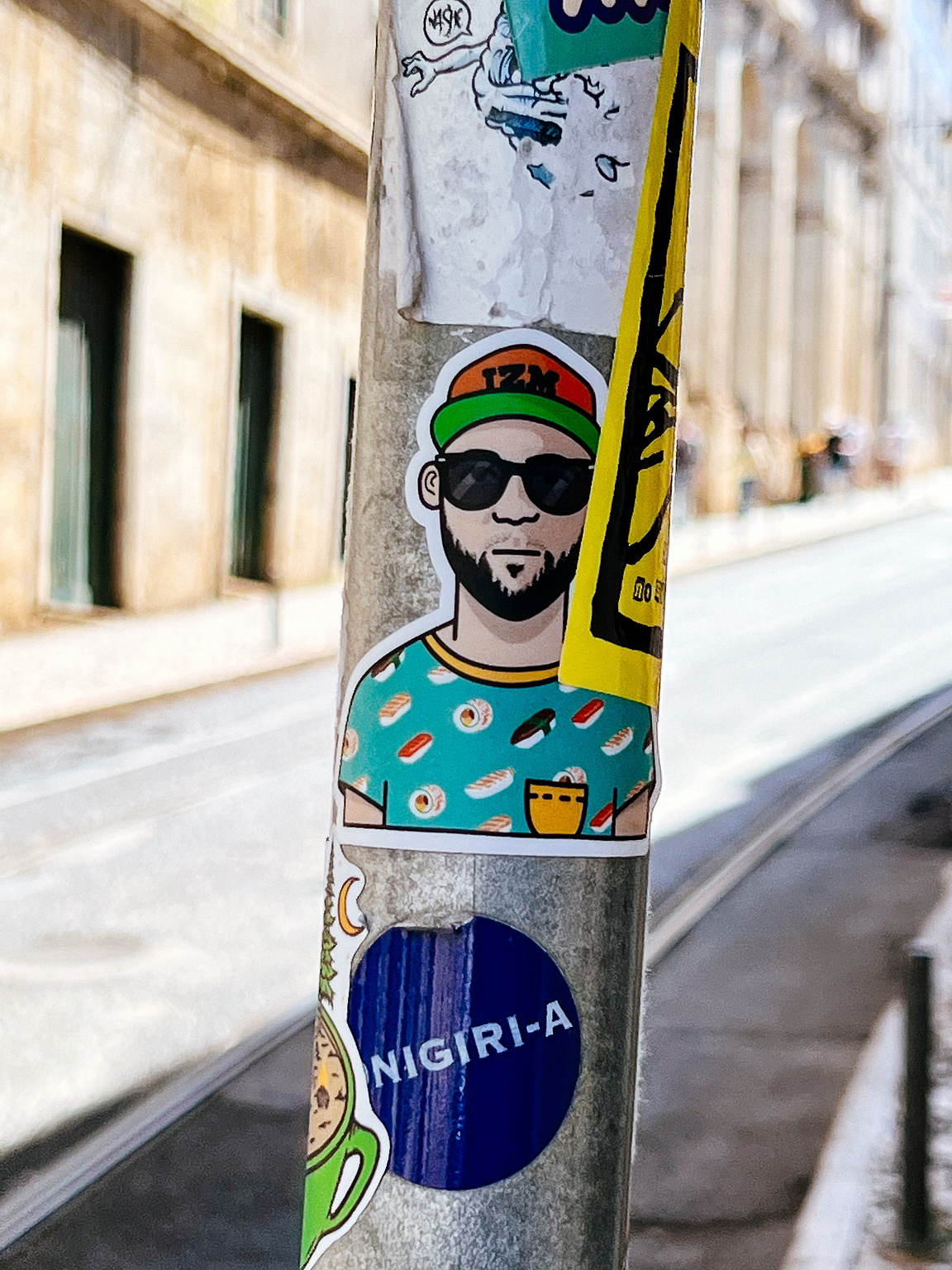 Stickers on a pole with a caricatured man wearing sunglasses and a cap, labeled "IZM", against an urban backdrop.