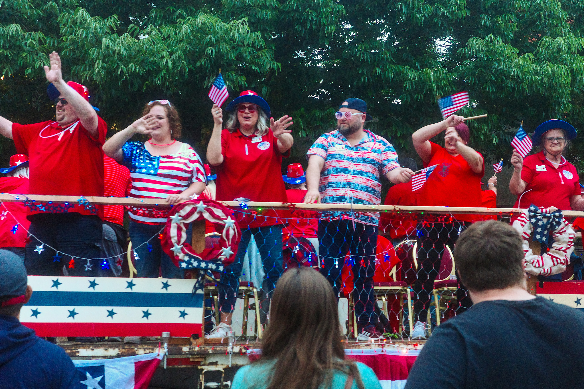 People on a float wearing a lot of flag regalia and waving at the crowd. 