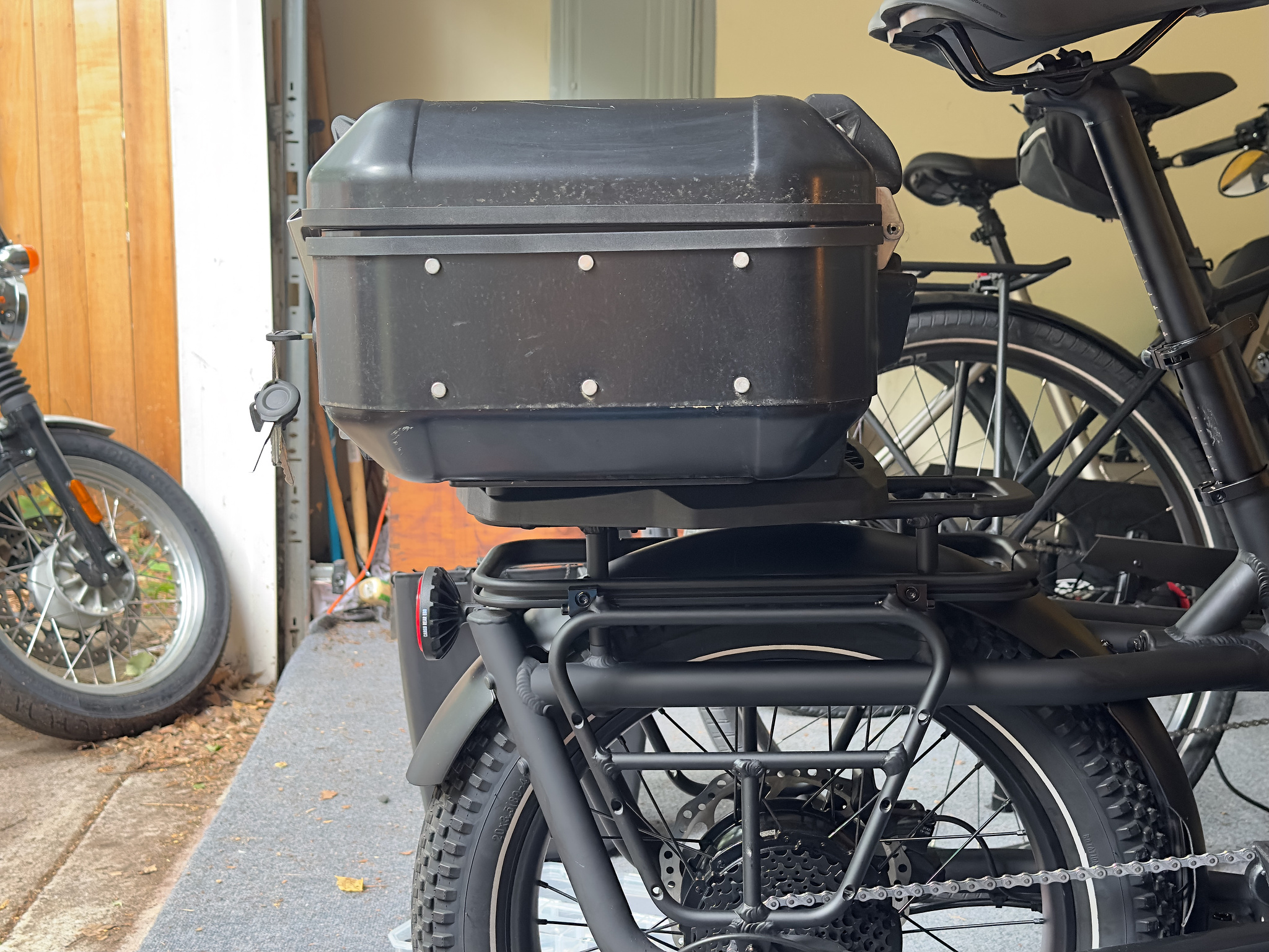 Side view of a black aluminum motorcycle top case mounted to the rear rack of a short-tail cargo bike. 