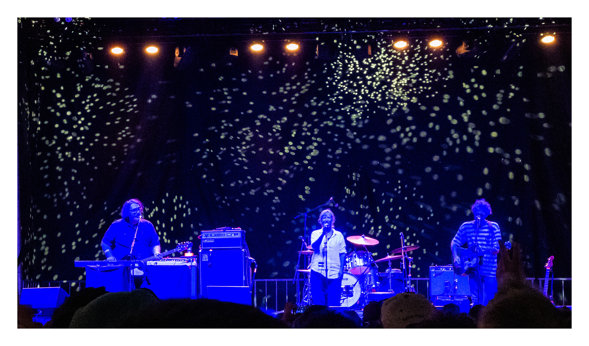 Yo La Tengo bathed in blue light with golden light dapples on the curtain behind them