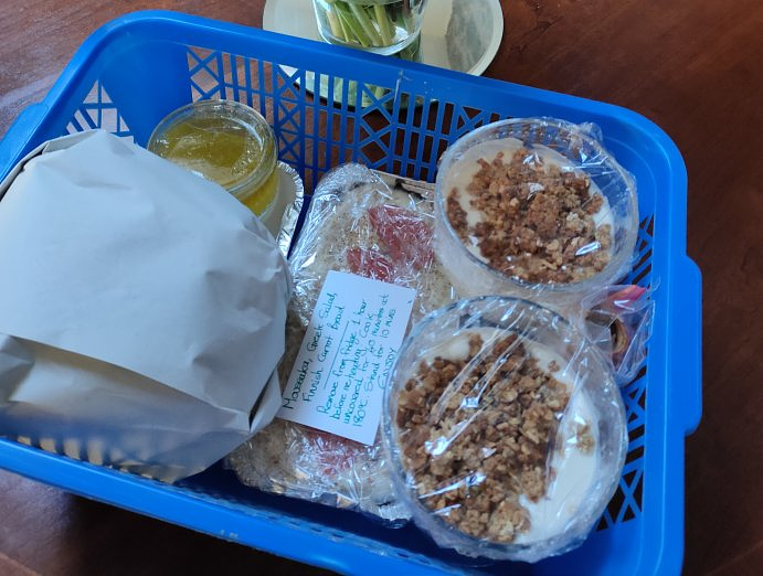 A blue basket containing various portions of food.  A lemon desert, some Moussaka, fresh bread and other things