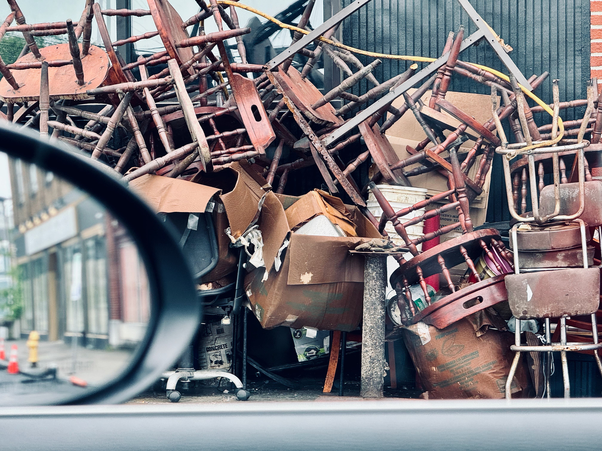 a crap load of chairs piled up for trash outside of a closed restaurant.