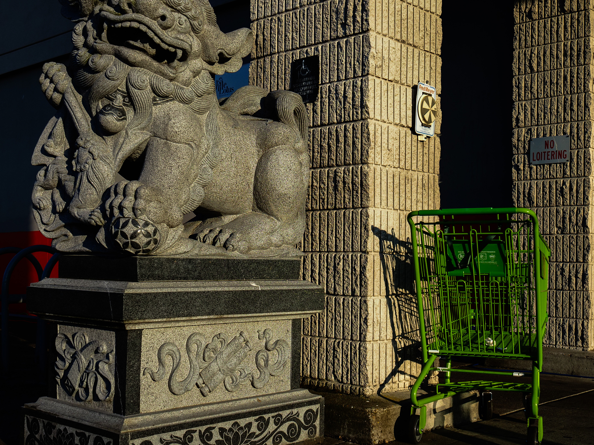 A green shopping cart next to a stone Chinese lion.