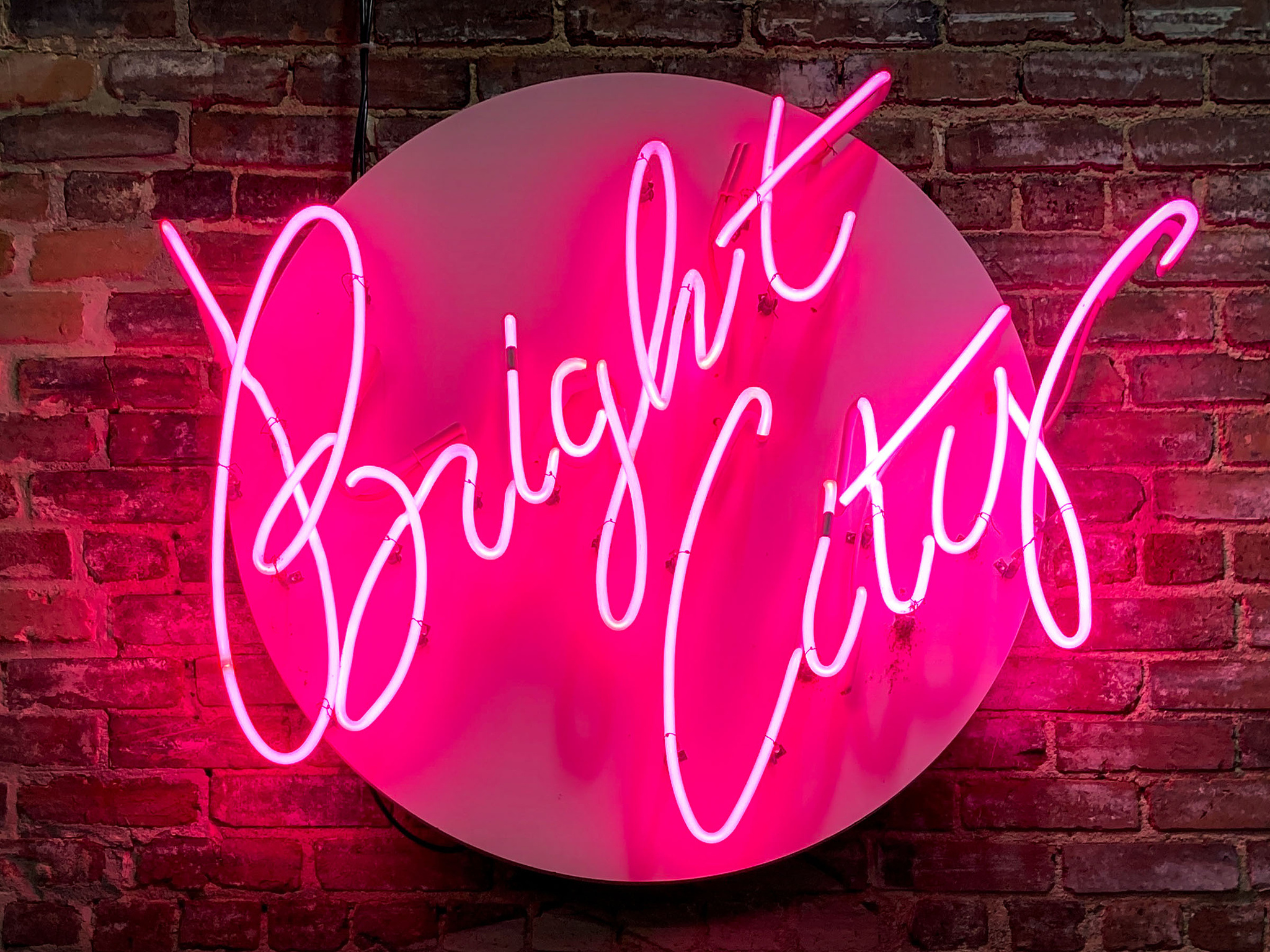 "Bright City" neon sign on brick wall.