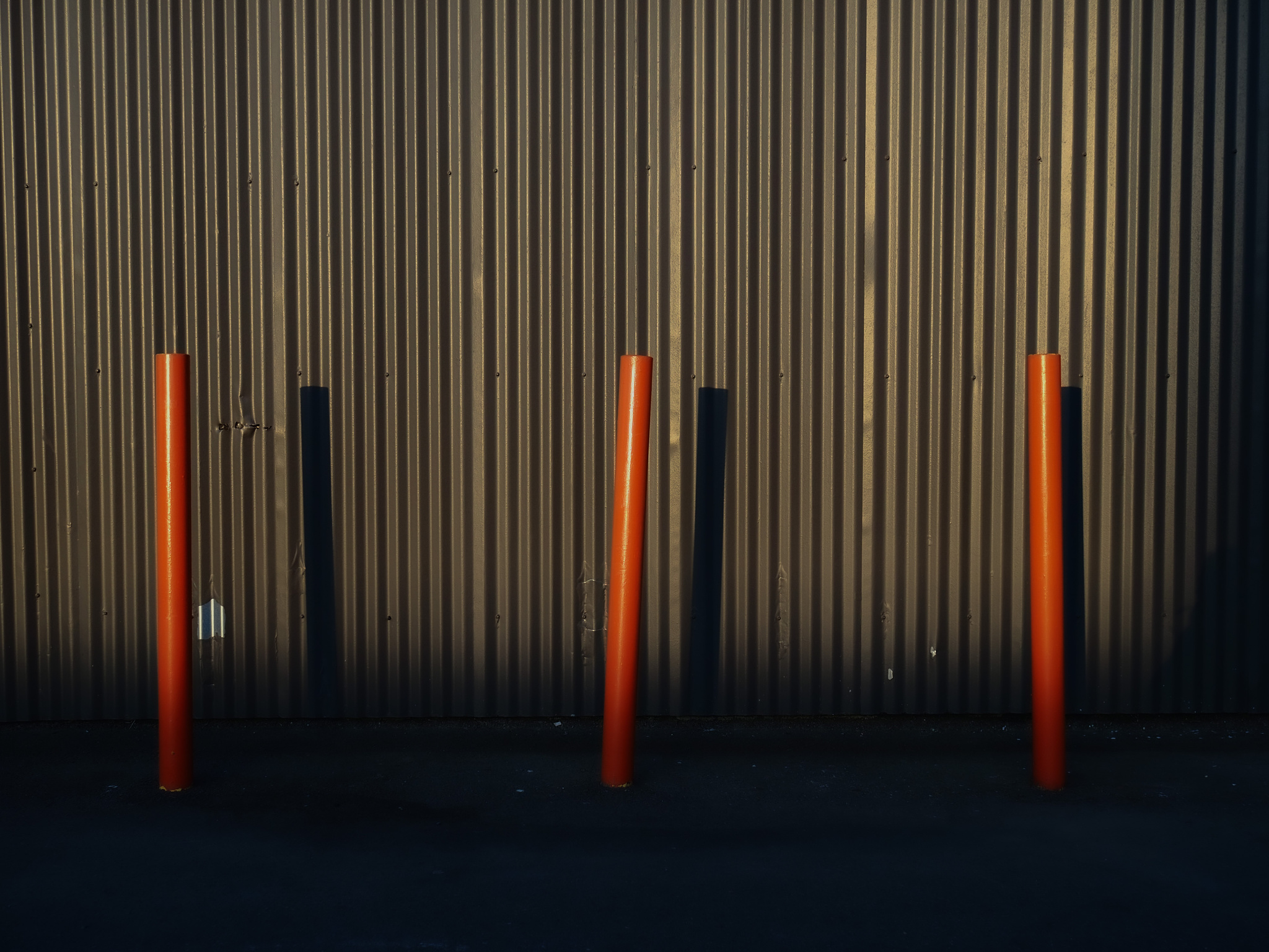 Orange bollards against a brown aluminum building. 