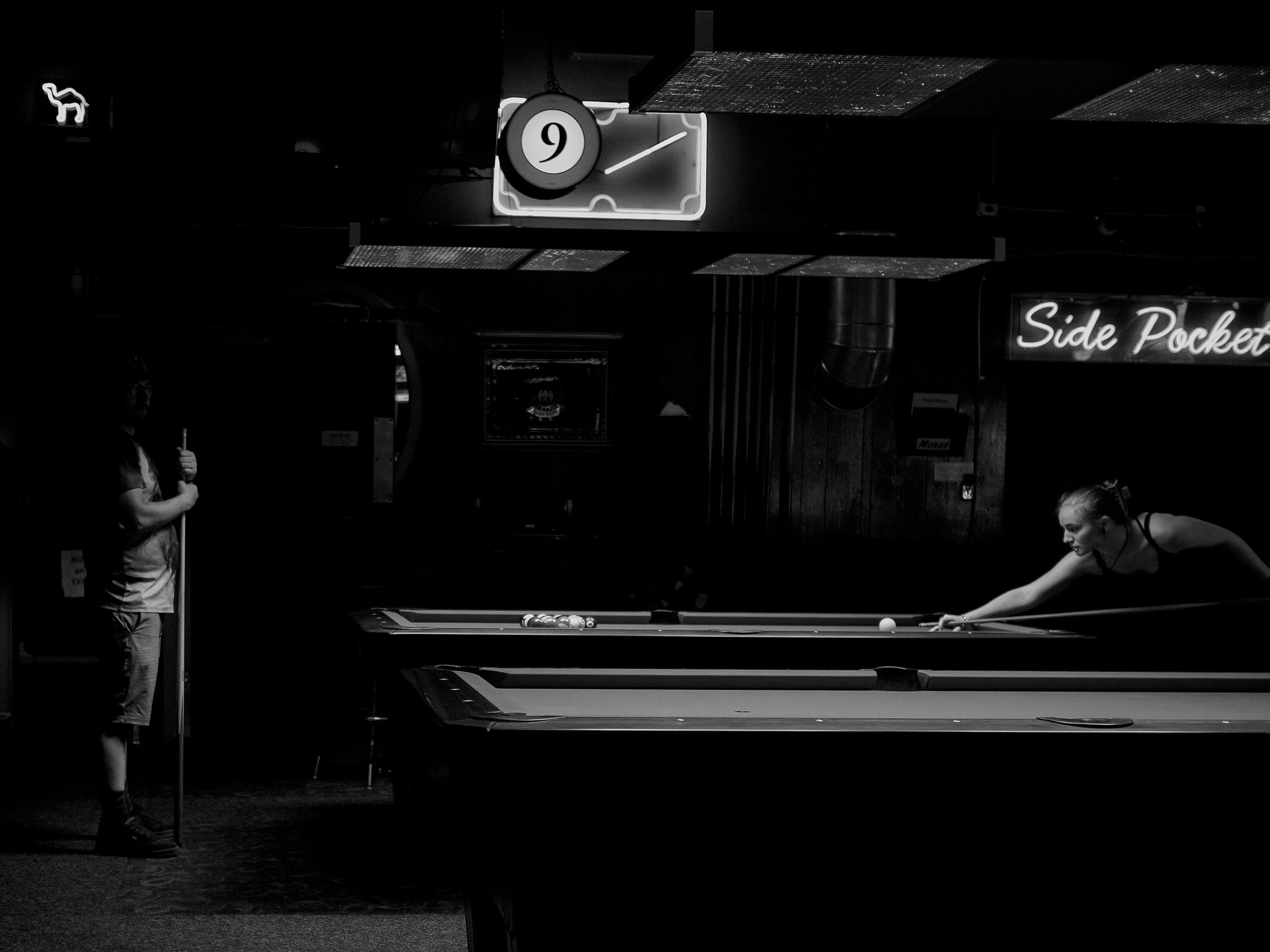 Monochrome. A woman at a pool table lines up the break. 