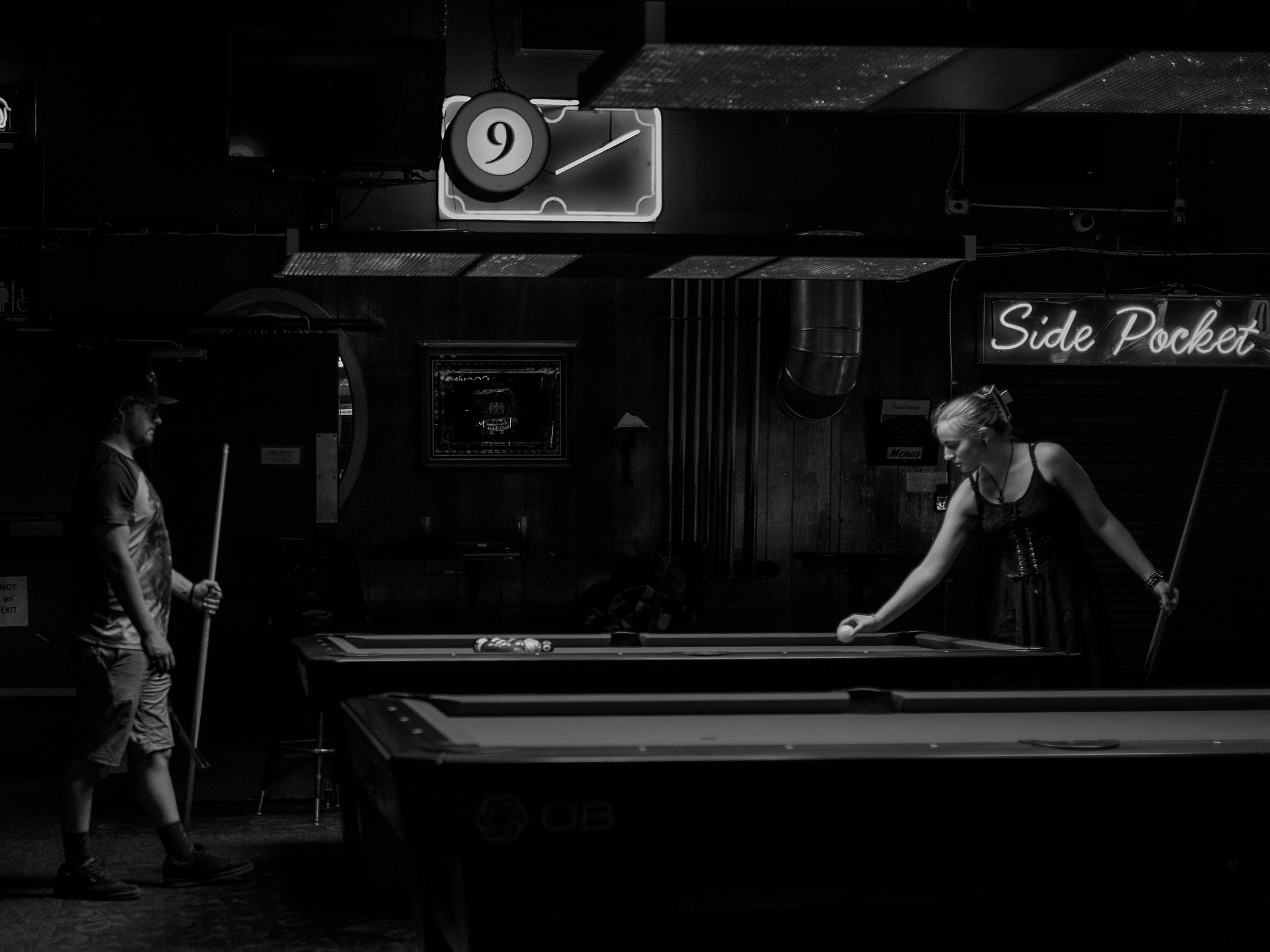 Monochrome. A woman sets a cue ball down on the table while her partner watches. 