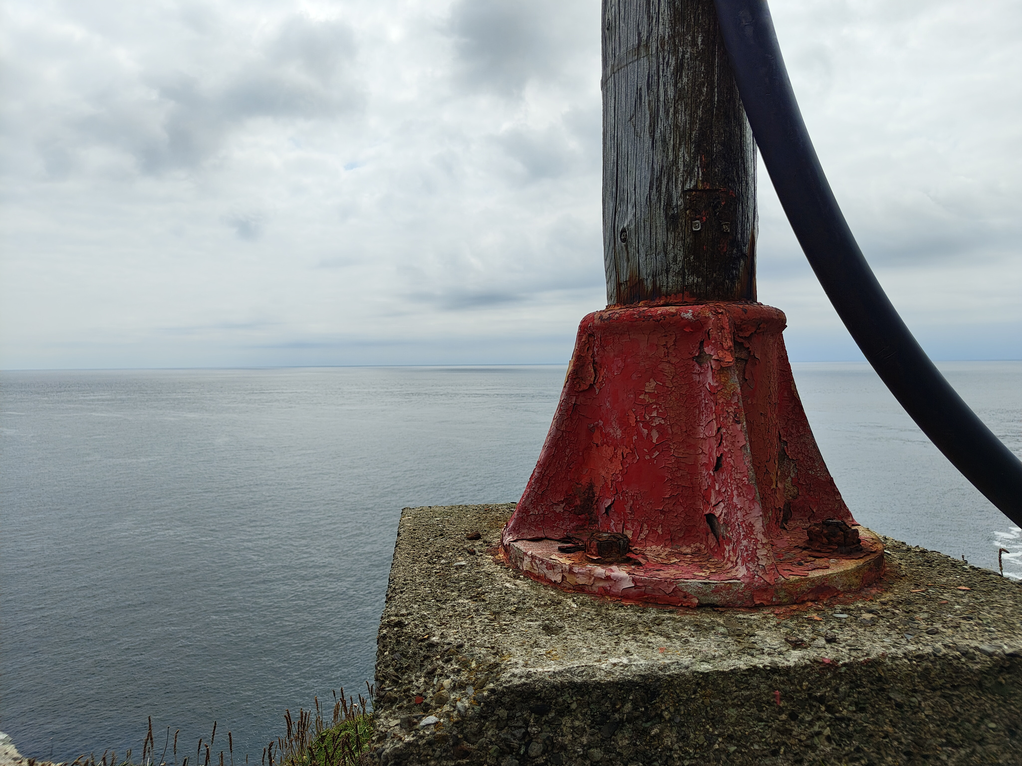 Red rust on a still red-painted post base looking out to sea