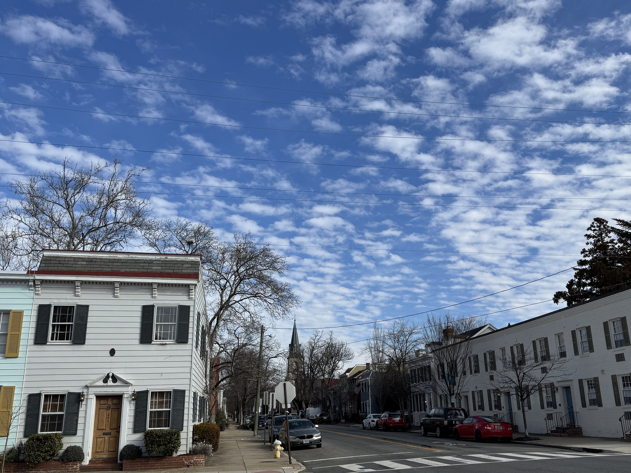 city street with historic townhomes and a church steeple in the back. crisp blue sky with dotted white clouds