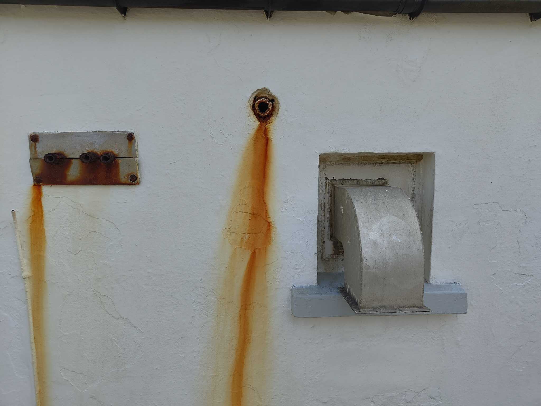 Red rust tails from iron pipes and vents coating a whitewashed wall