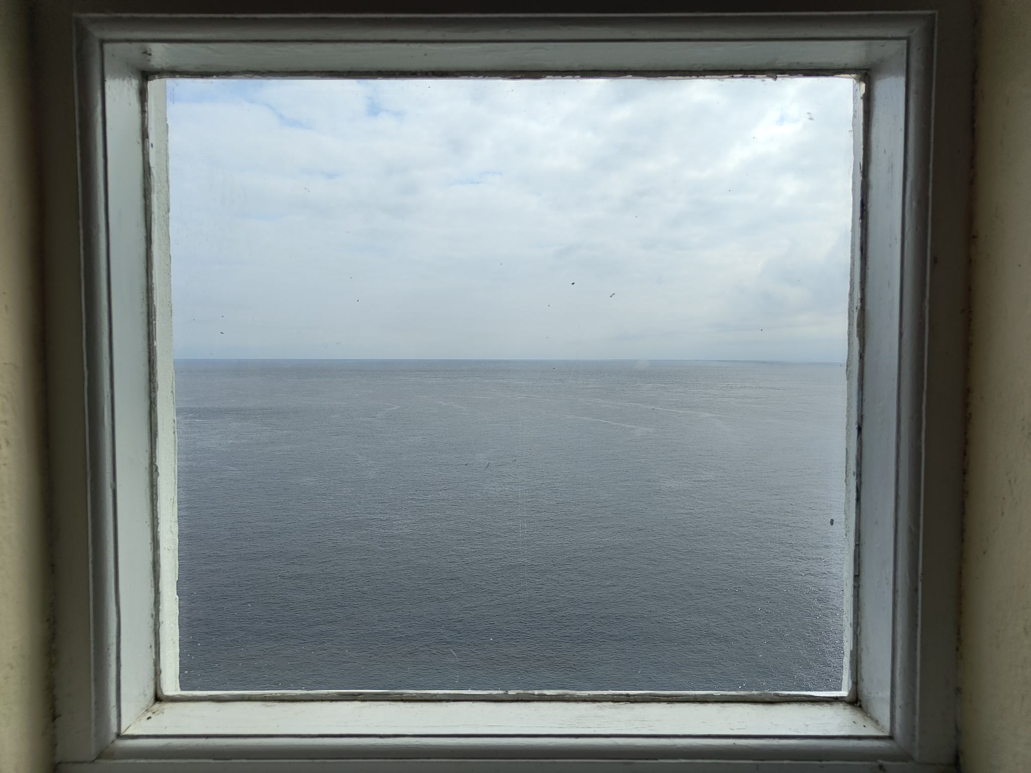 The view of a calm, grey sea from an old, slightly misted and mildewed, white-paned window