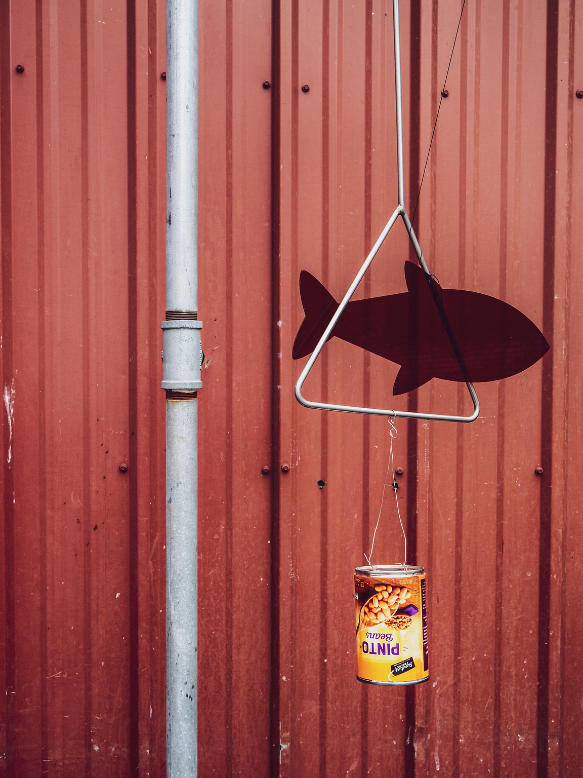 An eyewash station against a red metal background. A can of beans and a plastic fish are suspended in the air