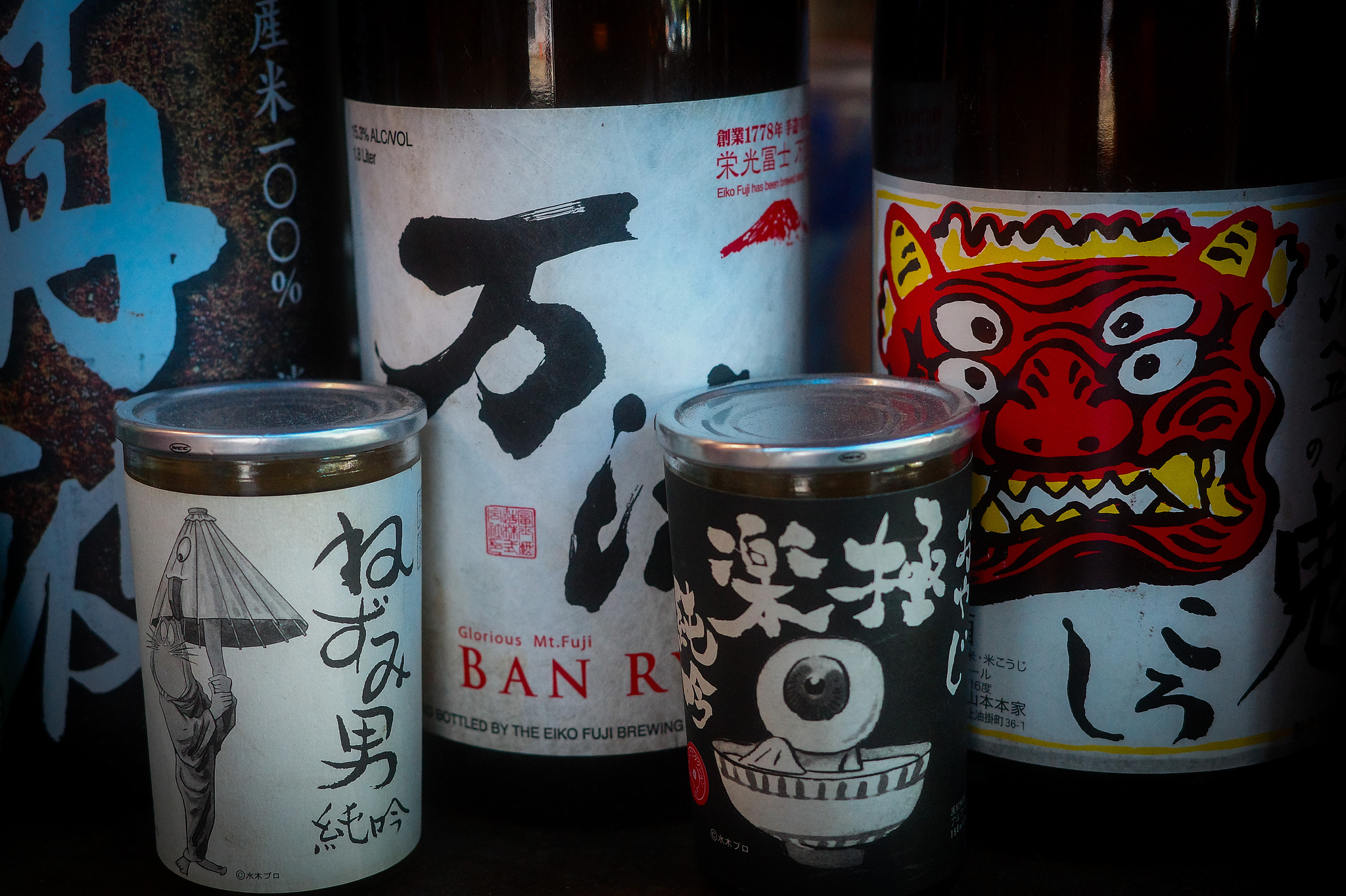 A collection of sake bottles close up, one with a bright red Noh  logo