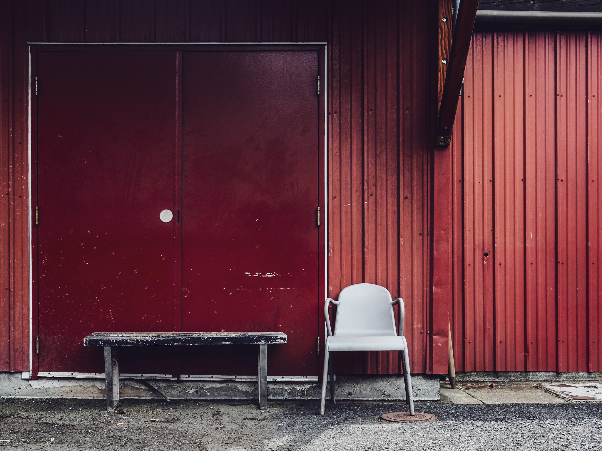 A bench and a gray plastic chair against a red corrugated metal building