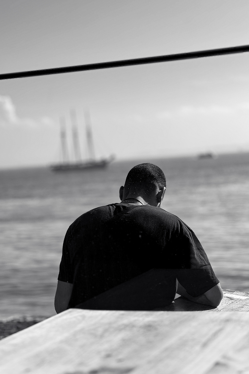 A person sits by the river. A boat in the background.