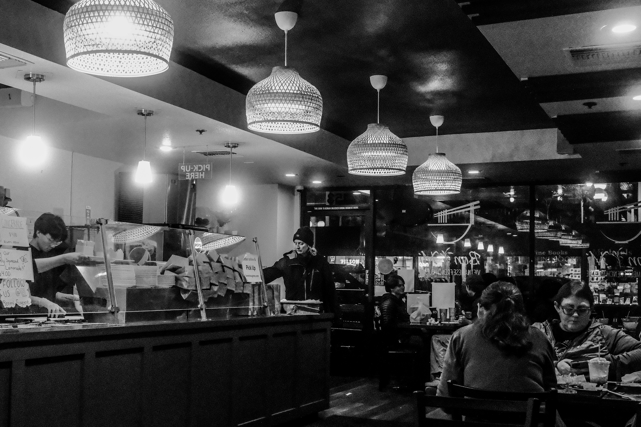 Monochrome. People in a brightly lit Pho restaurant. 