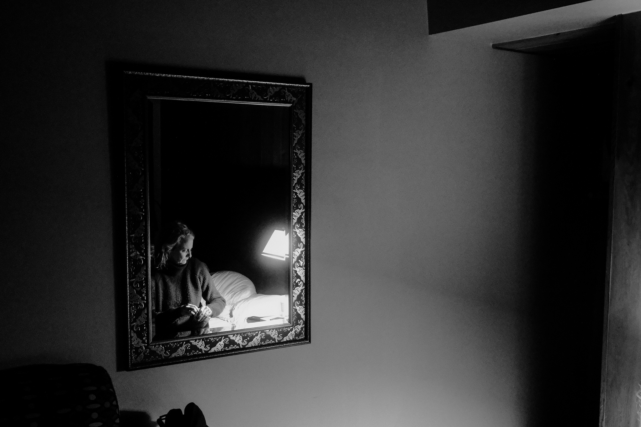 Monochrome. A woman sits on a bed, reflected in a mirror