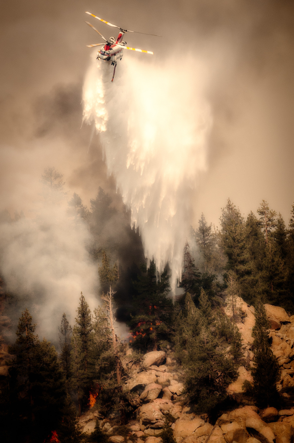 Fire fighting helicopter dropping water on a forest fire in the hills.