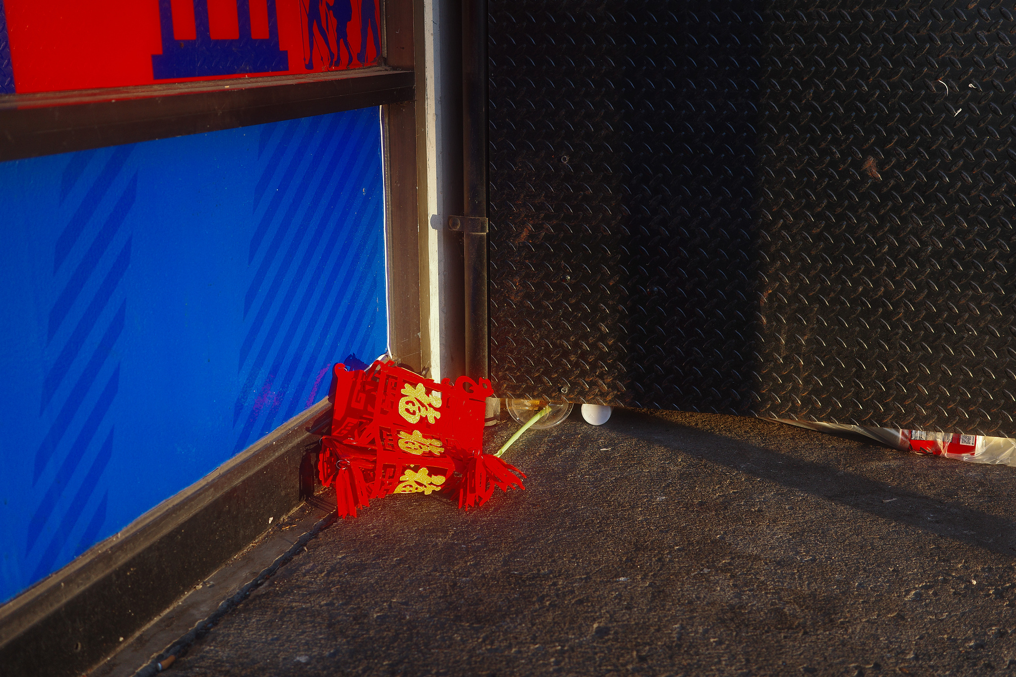 A red decorative Chinese lantern resting on the concrete, against a bright blue wall. 