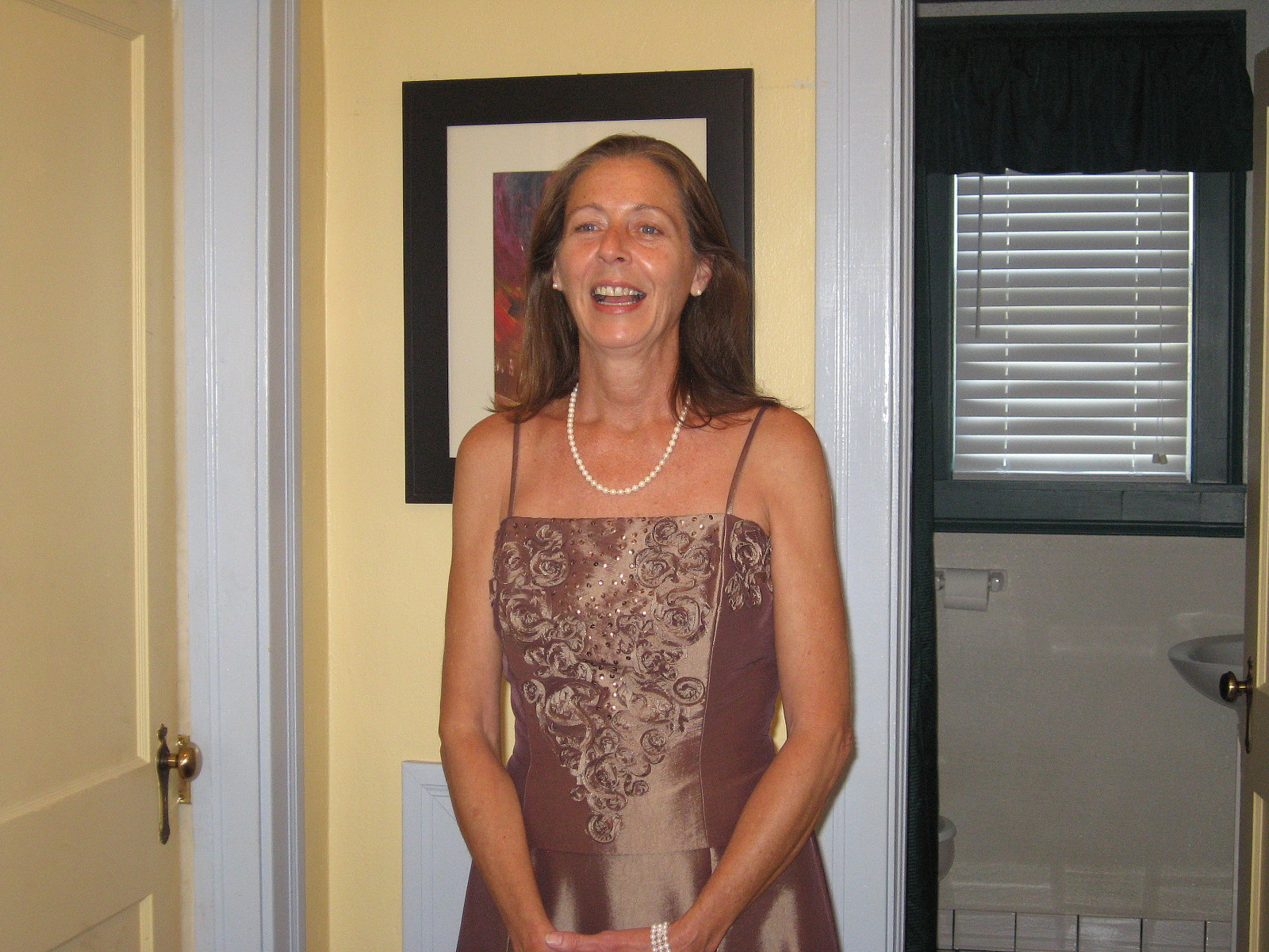 A woman in a brown dress and wearing pearls. 