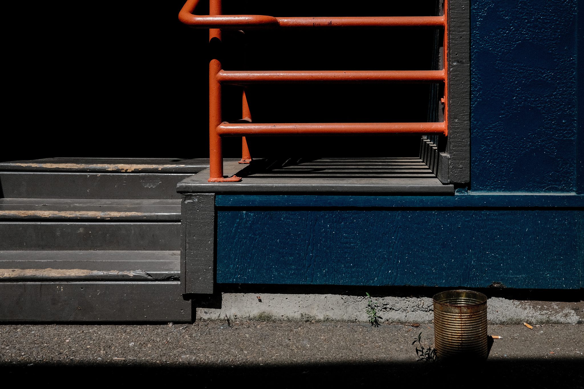 Orange handrails against a blue wall. A coffee can for cigarettes on the ground.