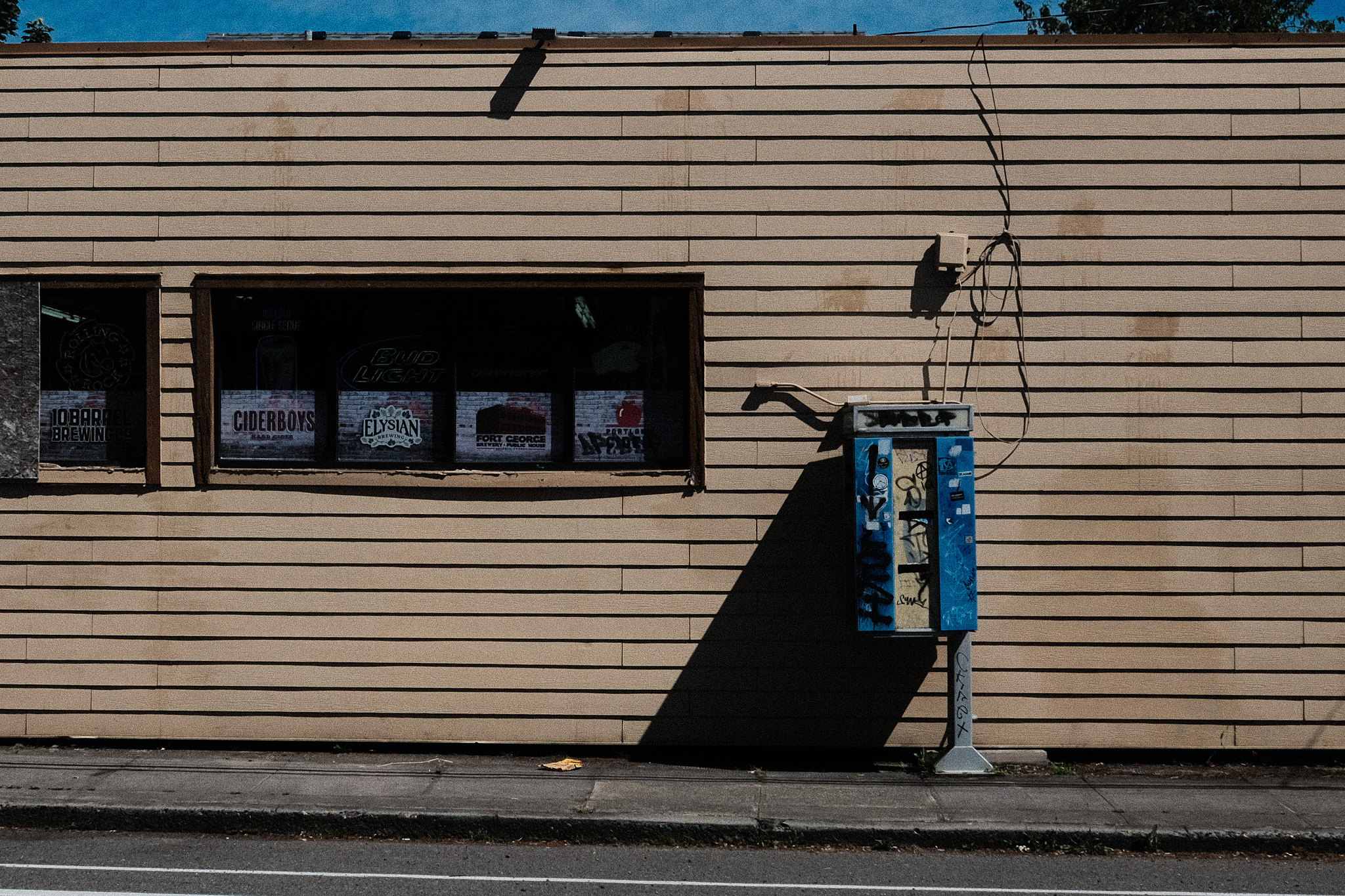 An old blue public phone against a brown building. 