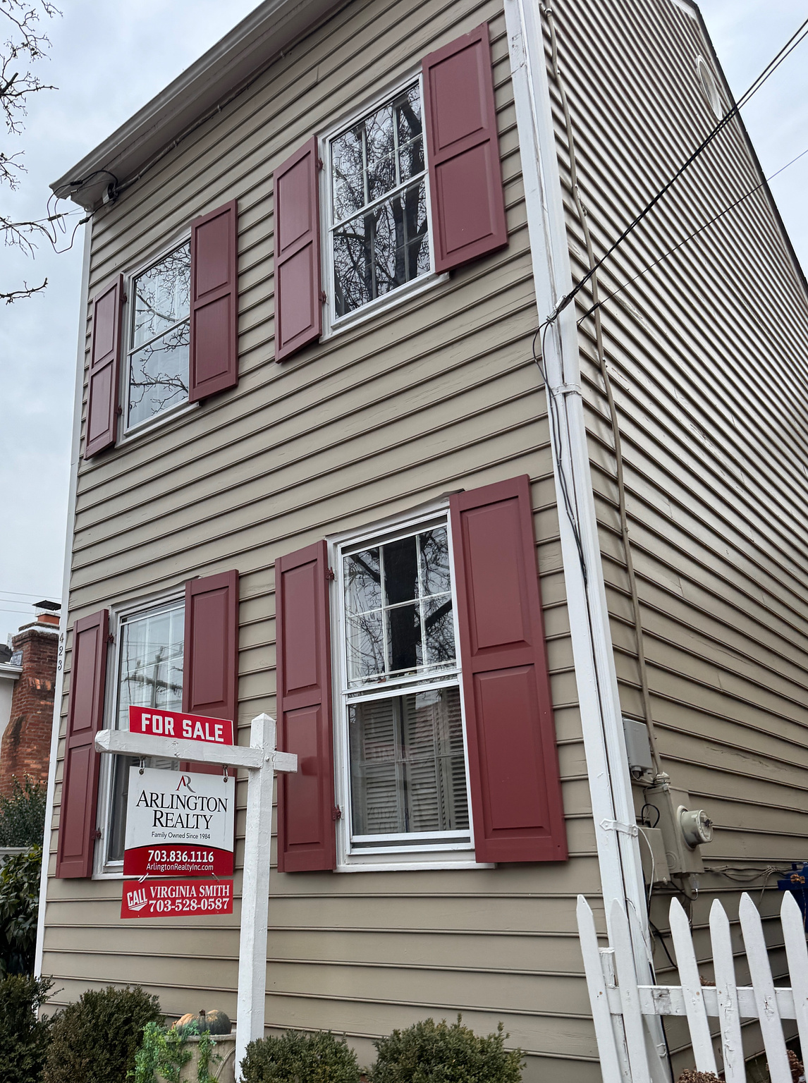 exterior of a tan townhouse with red shutters and a for sale sign