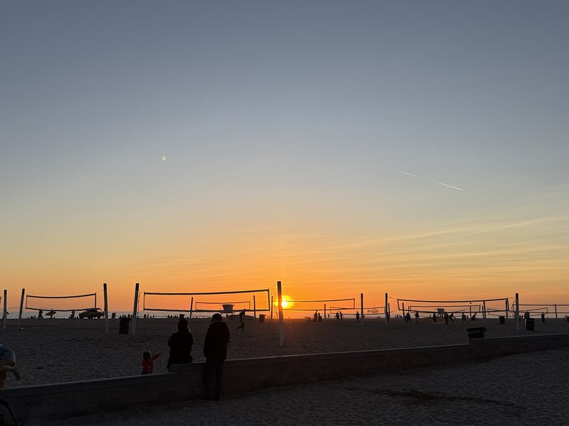 Sun setting over the ocean with volleyball nets in the foreground and the beach in the background