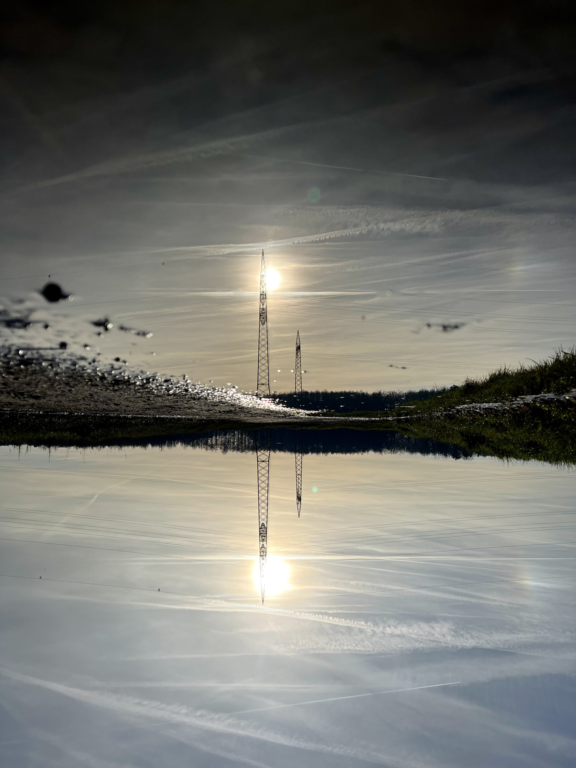 A puddle on a path between fields. in the puddle you see the reflectionof the winter sun behind a power pole. Zhe whole picture is turned upsidedown.