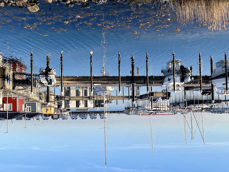 Small boats in a harbour, reflected in the blue water. The picture is turned upside down.
