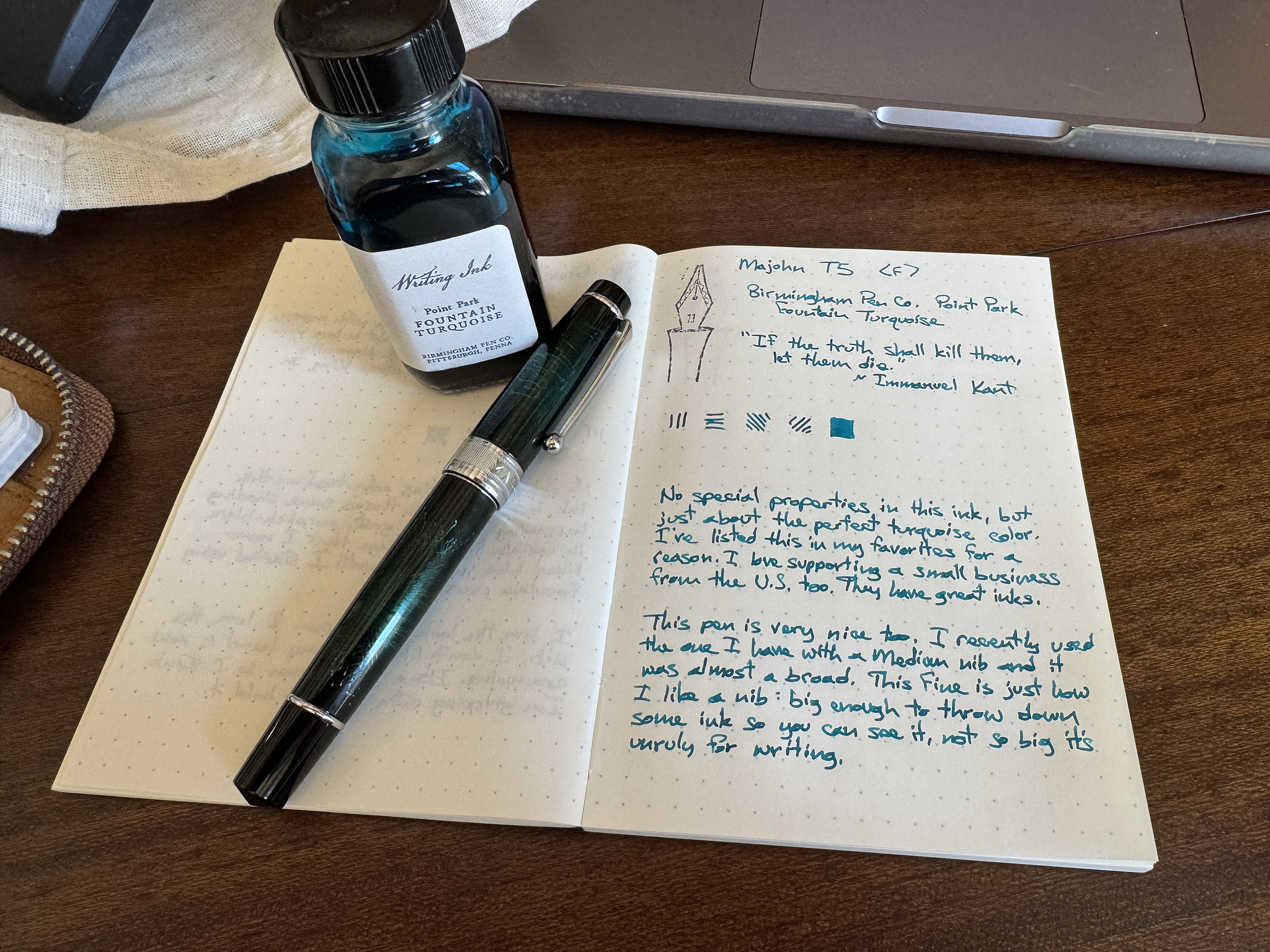 bottle of turquoise fountain pen ink, a green fountain pen with silver trim, and a writing sample in an open notebook