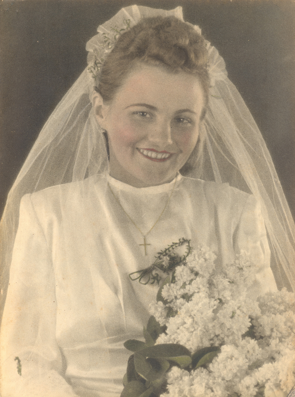 A young woman in a 1940s-style white wedding dress and veil, smiling warmly while holding a large bouquet of white flowers. She wears a gold cross necklace and has a soft, vintage glow to her appearance.
